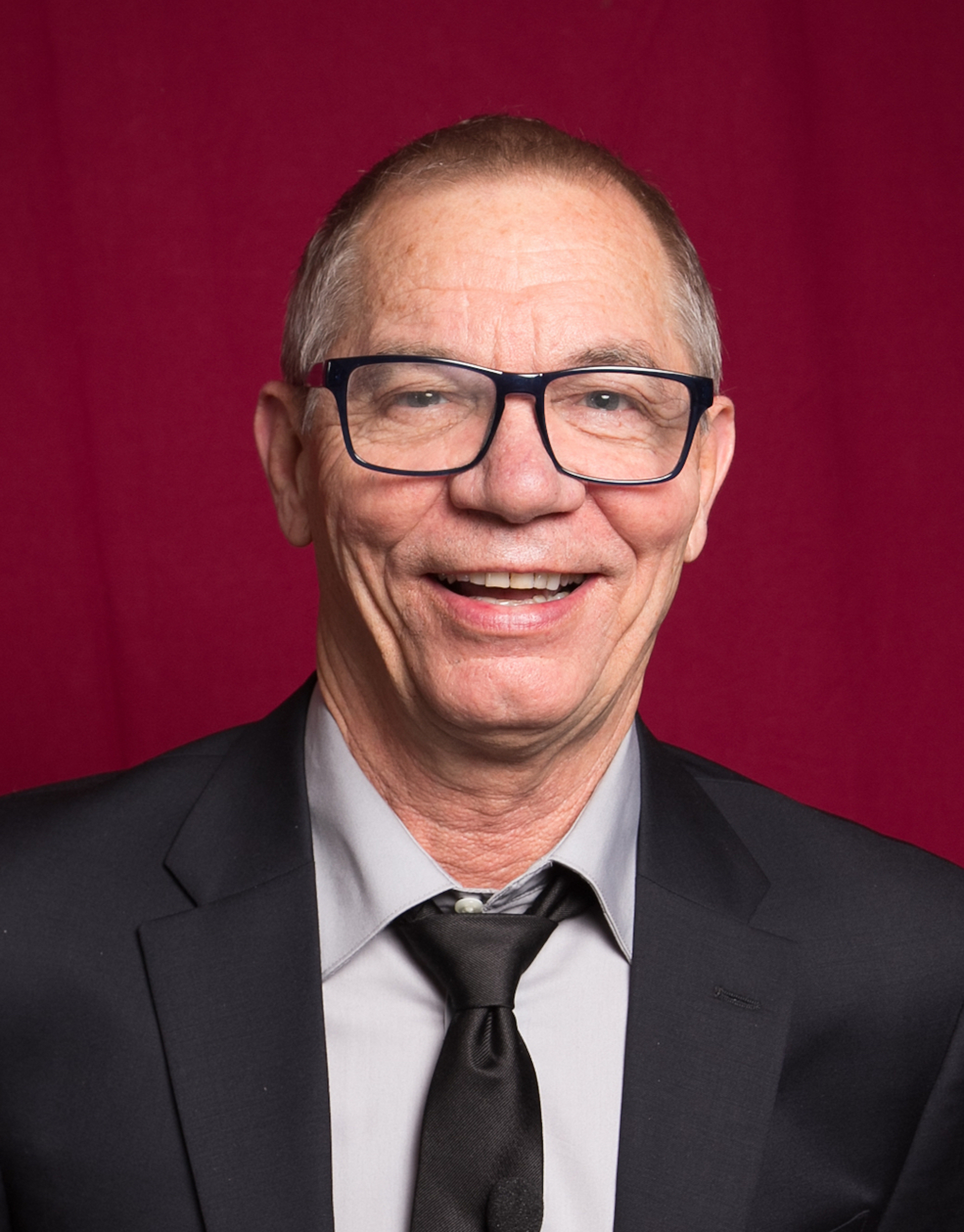 man with black glasses in front of a red background